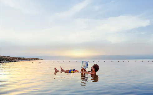 Person floating and reading in the Dead Sea during sunset on a half-day trip from Amman.