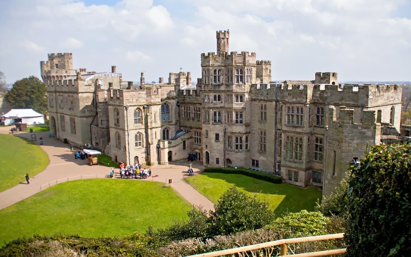 Warwick Castle facade with visitors exploring the historic stone architecture.