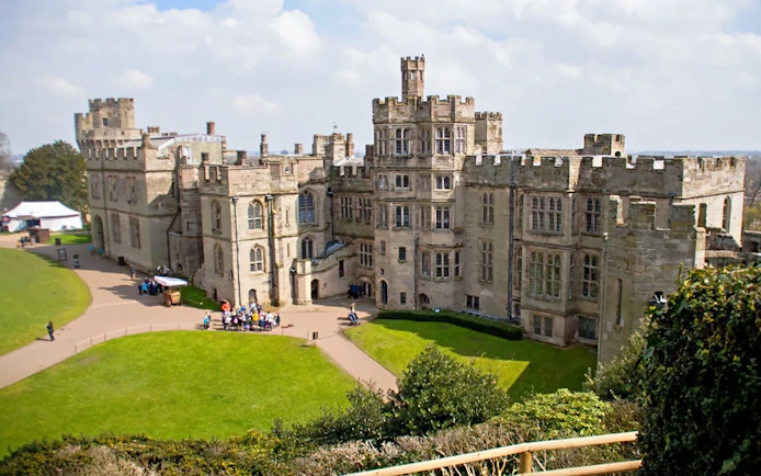 Warwick Castle facade with visitors exploring the historic stone architecture.