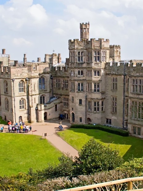 Warwick Castle facade with visitors exploring the historic stone architecture.