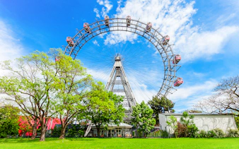 Blumenrad Ferris Wheel in Vienna with lush green trees and blue sky.