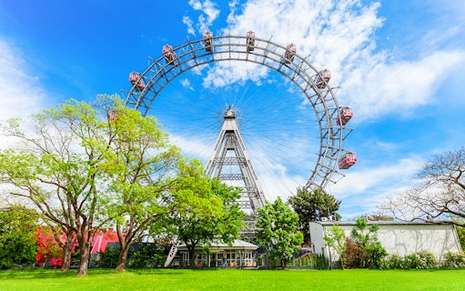 Blumenrad Ferris Wheel in Vienna with lush green trees and blue sky.