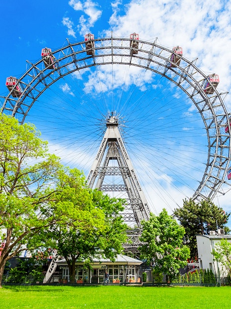 Blumenrad Ferris Wheel in Vienna with lush green trees and blue sky.