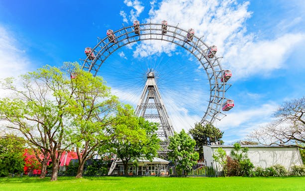 Blumenrad Ferris Wheel in Vienna with lush green trees and blue sky.