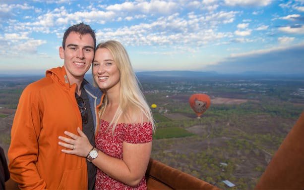Couple enjoying a hot air balloon ride over Cairns with scenic landscape views.