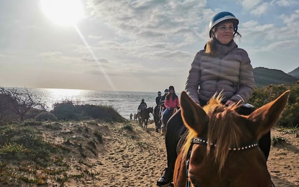 Horseback riders on a sandy trail by the sea in Porto Ferro, Sardinia.