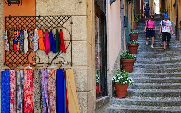 Colorful scarves and ties displayed on a wall in Bellagio, with tourists walking down stone steps.