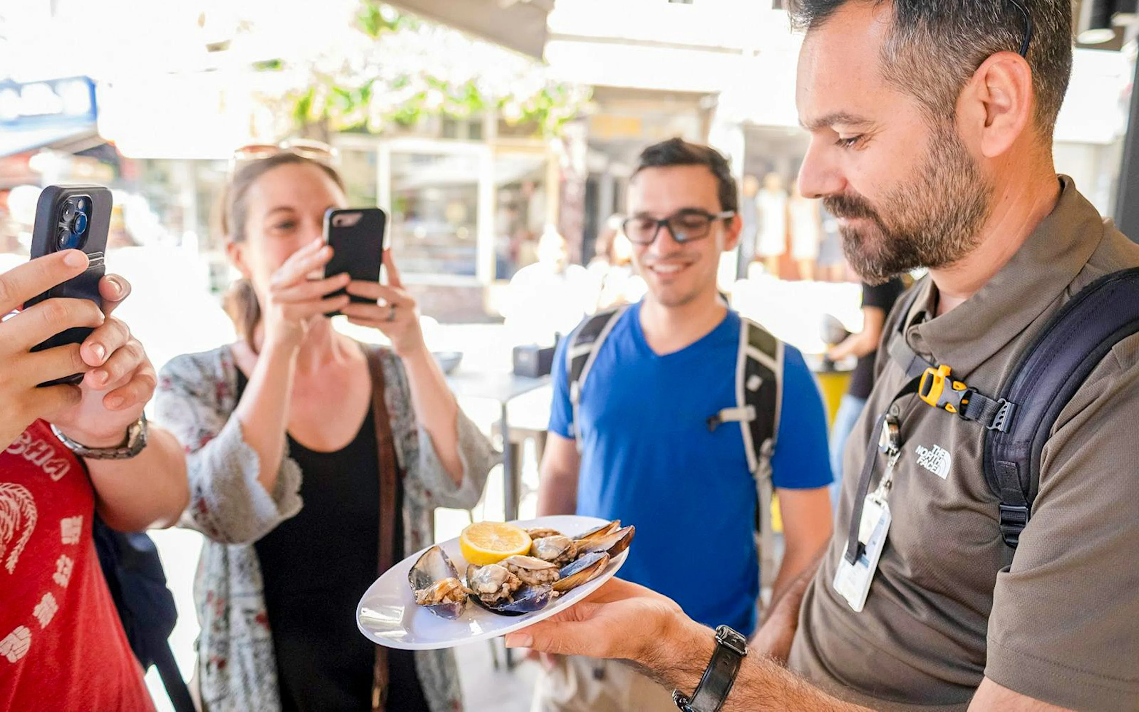 Tour guide presenting a plate of mussels with lemon to tourists on the Taste of Two Continents Food Tour.