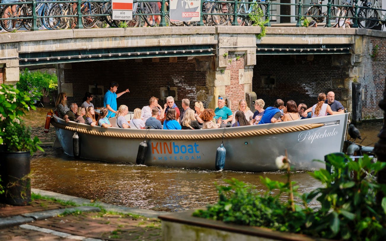 Open boat with tourists cruising under a bridge on Utrecht canal.