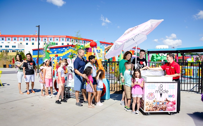 Guests enjoying ice cream at Legoland New York with colorful buildings in the background.