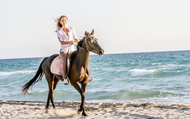 Horse riding along Antalya beach with ocean waves in the background.