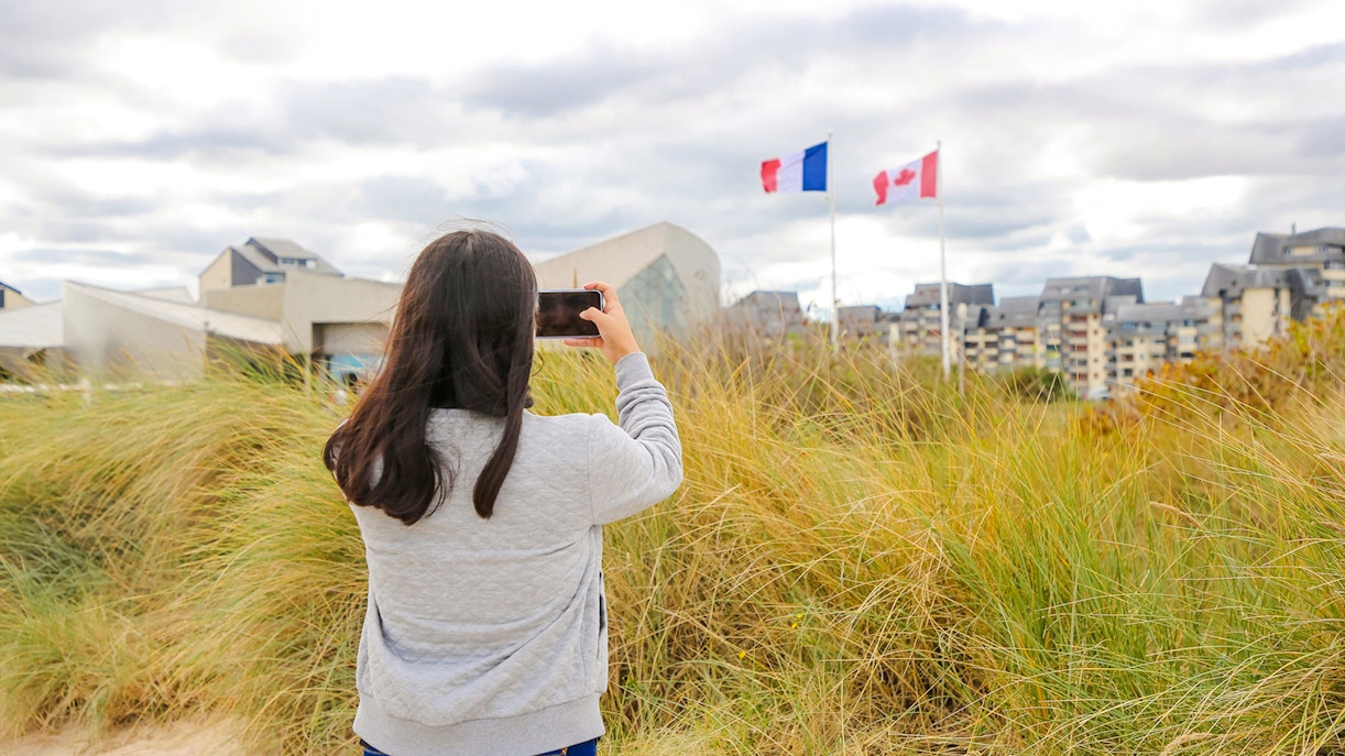 Visitor photographing flags at Juno Beach Centre, Normandy, France.