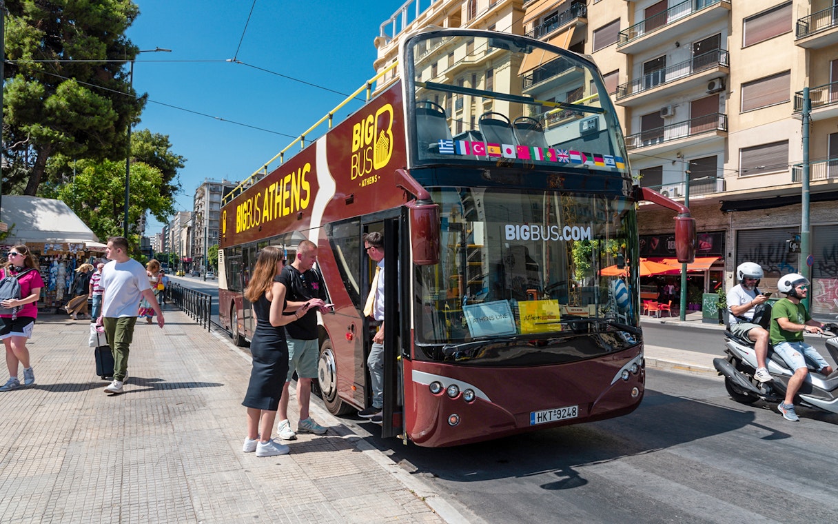 Hop-on hop-off bus in Athens with tourists boarding near city street.