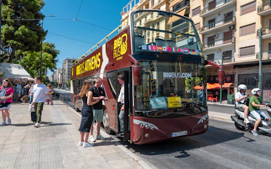 Hop-on hop-off bus in Athens with tourists boarding near city street.