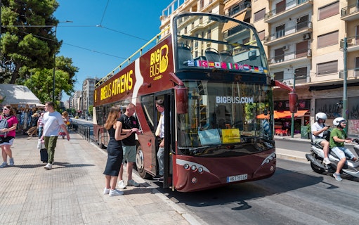 Hop-on hop-off bus in Athens with tourists boarding near city street.