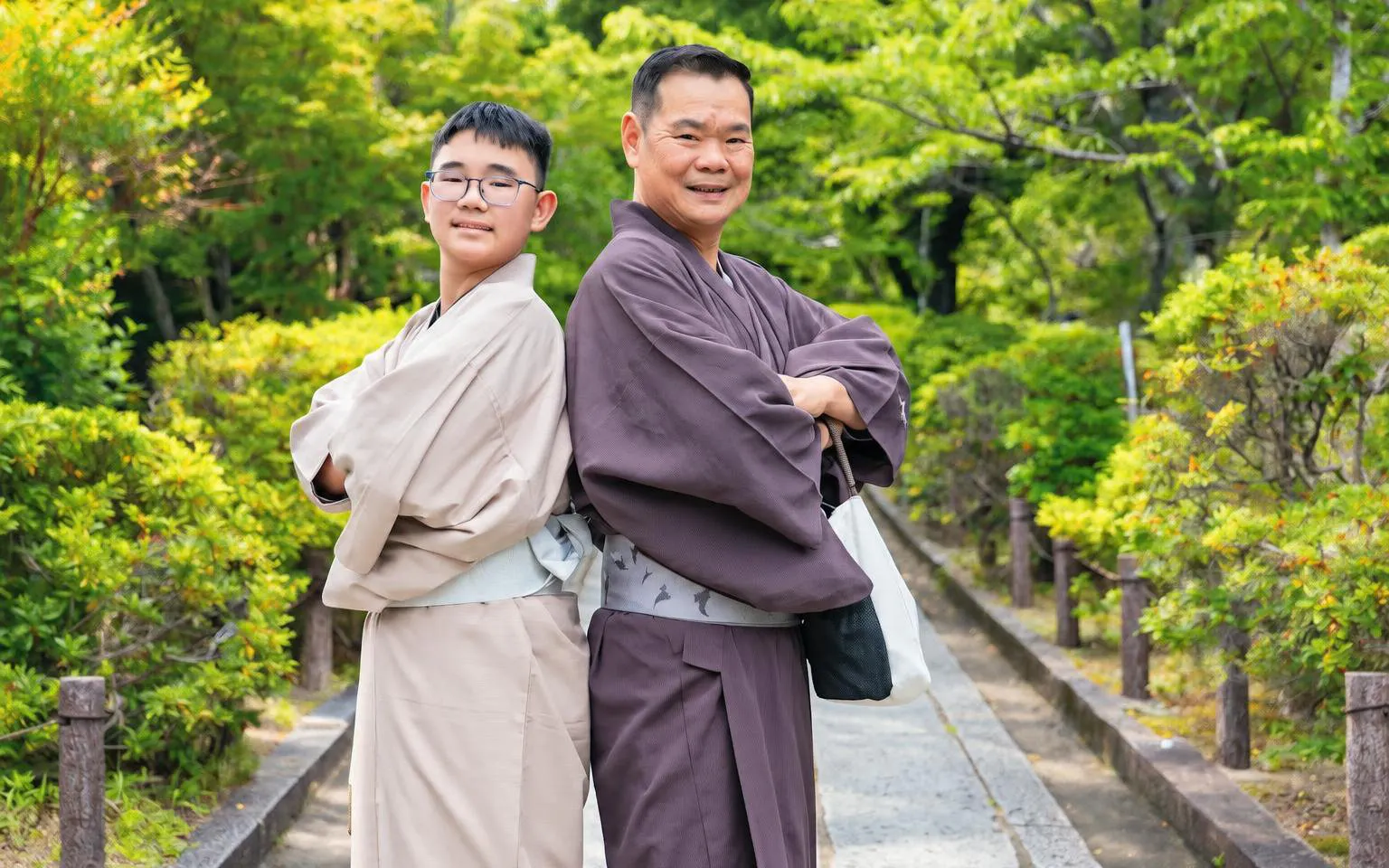 Men wearing traditional kimonos in a Kyoto garden pathway.