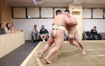 Sumo wrestlers competing in a Shibuya arena with an audience watching in Tokyo.