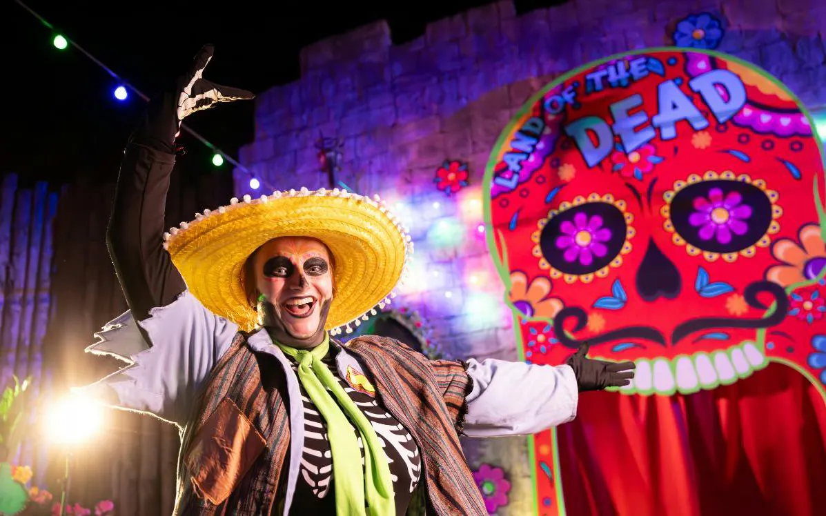 Performer in skeleton costume at Alton Towers Scarefest with colorful "Land of the Dead" backdrop.