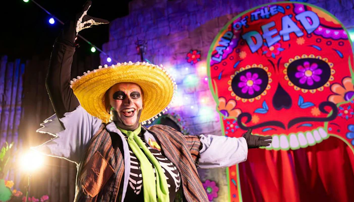 Performer in skeleton costume at Alton Towers Scarefest with colorful "Land of the Dead" backdrop.
