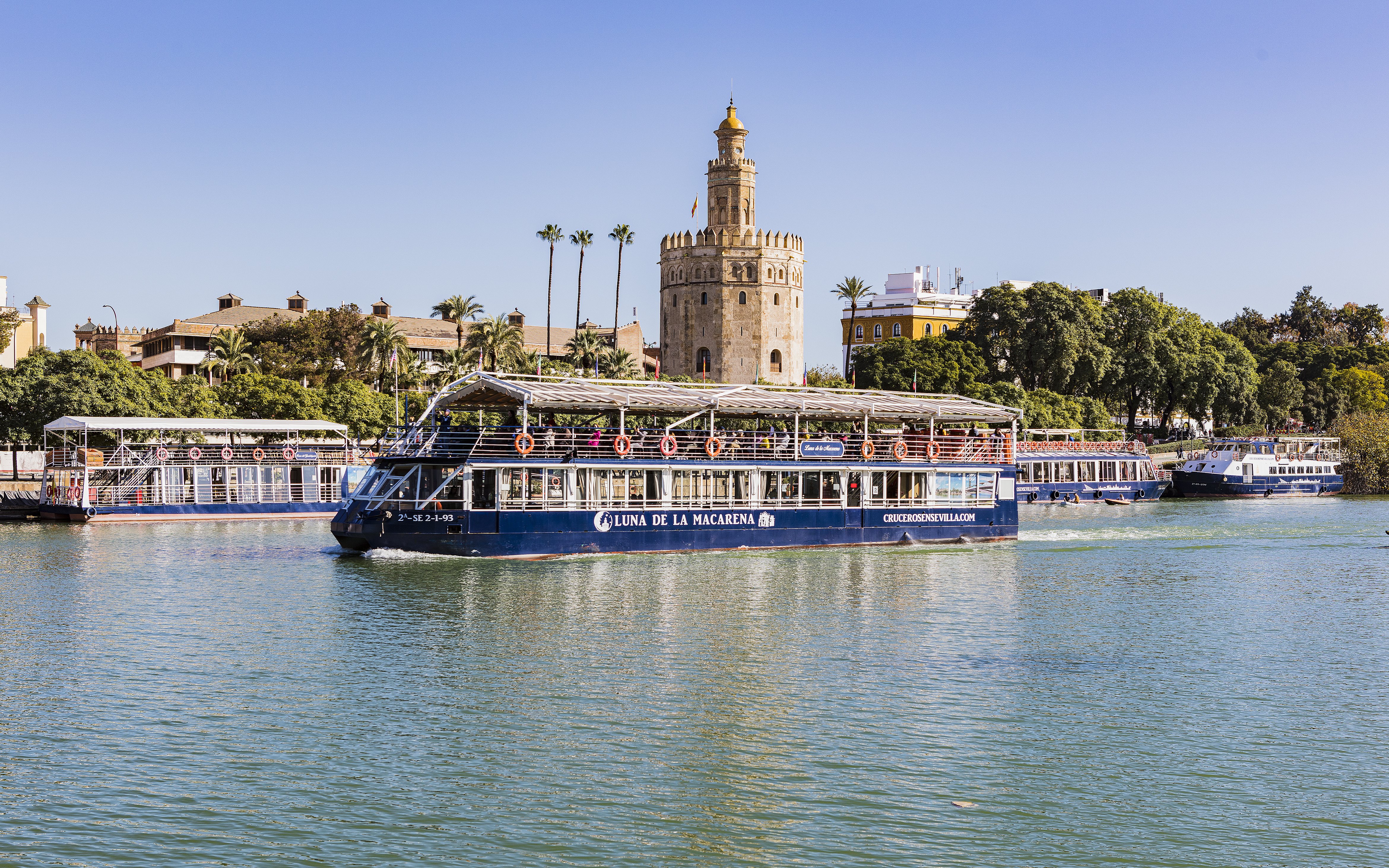 Cruise boat on Guadalquivir River passing Torre del Oro in Seville.