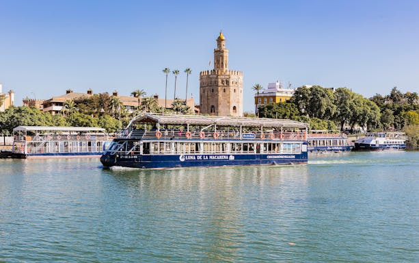 Cruise boat on Guadalquivir River passing Torre del Oro in Seville.
