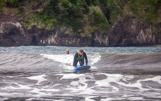 Surfer learning on waves at Madeira Island with lush cliffs in the background.