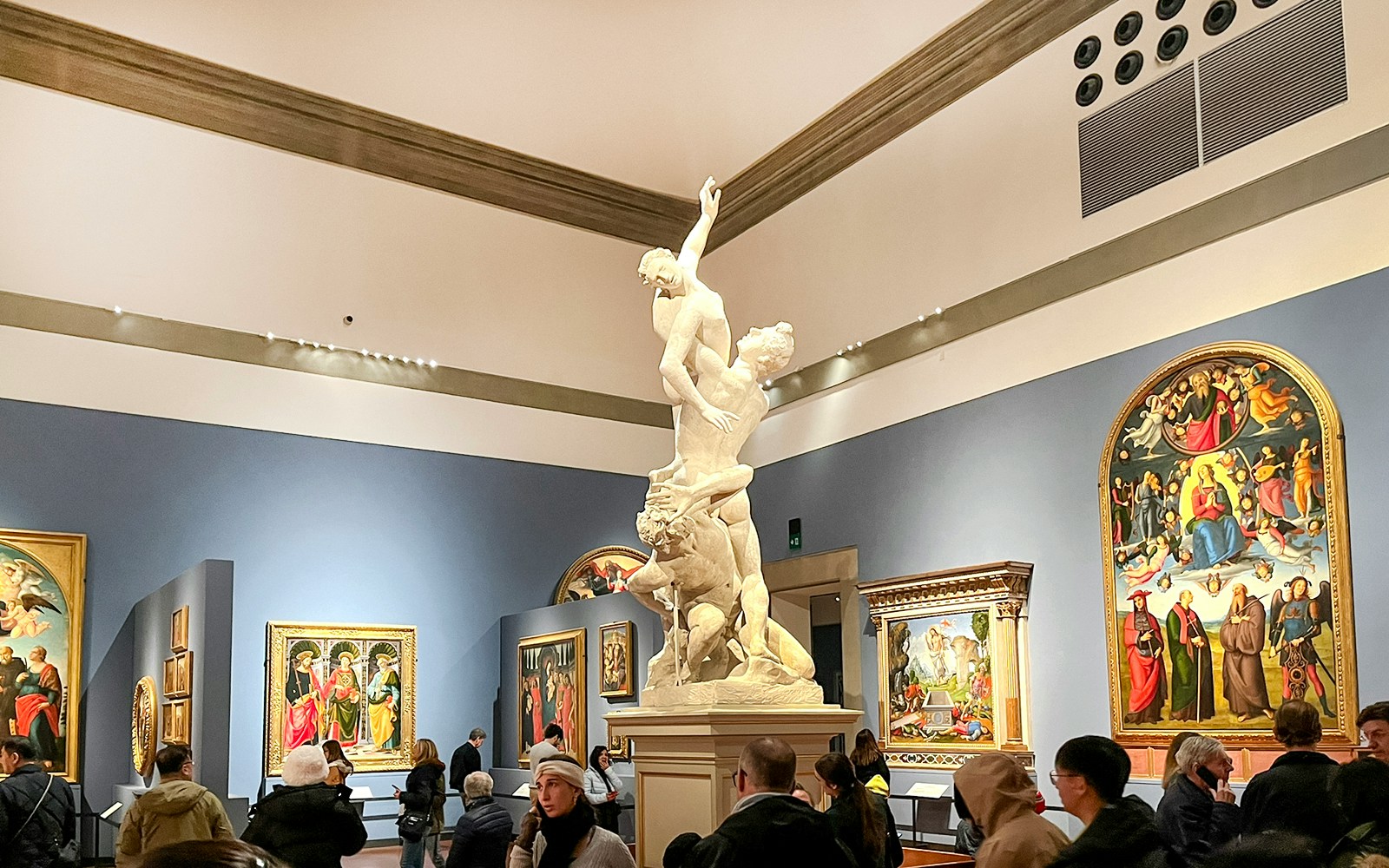 Sculpture in Hall of the Colossus, Accademia Gallery, Florence, with visitors viewing paintings.