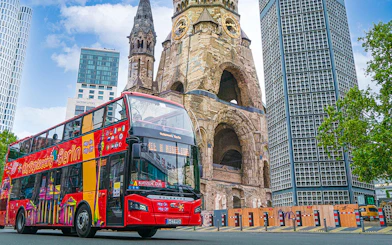Red double-decker bus on Berlin Hop On & Hop Off tour near Kaiser Wilhelm Memorial Church.