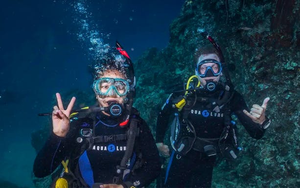 Beginners scuba diving in Maui, two divers underwater near coral reef.