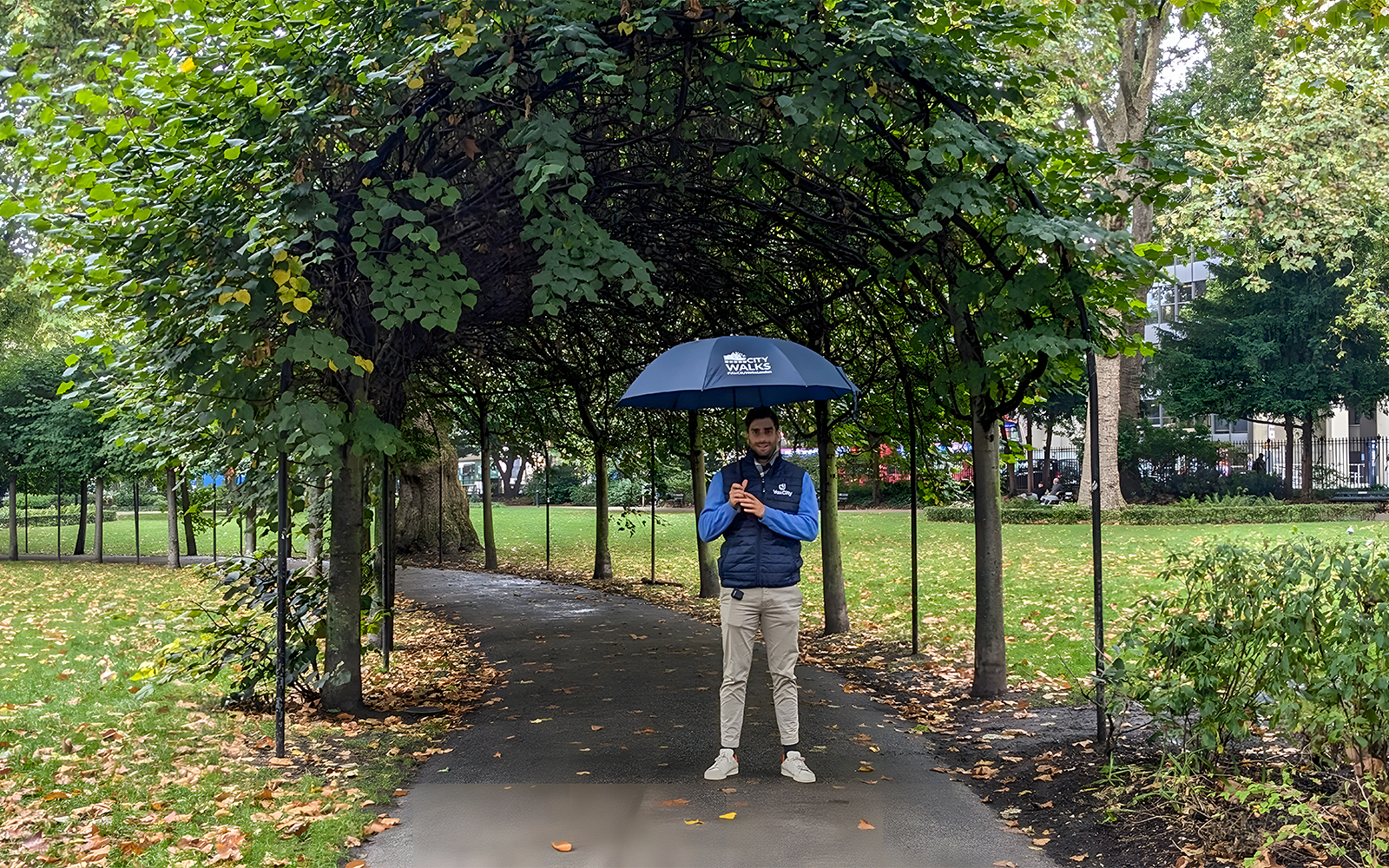 Guide holding an umbrella in a leafy park near the British Museum.