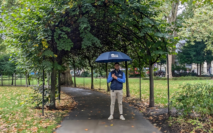 Guide holding an umbrella in a leafy park near the British Museum.
