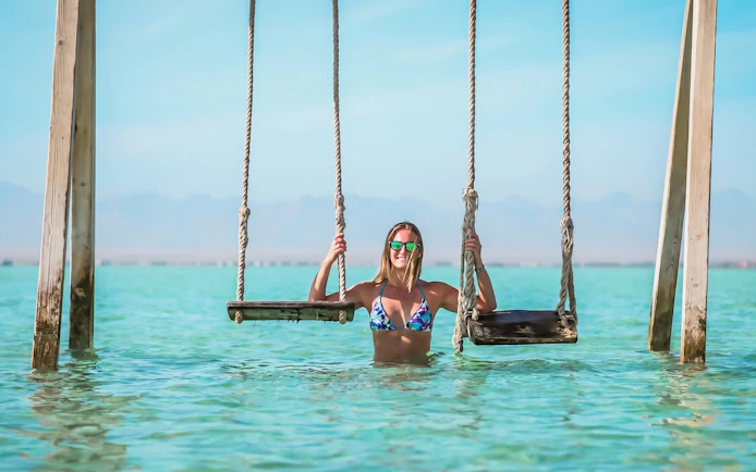 Person enjoying swings in clear water at Orange Bay, Giftun Island, Hurghada.