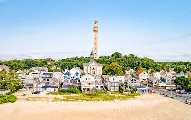 Pilgrim Monument towering over Provincetown, Cape Cod, with colorful houses and sandy beach in foreground.