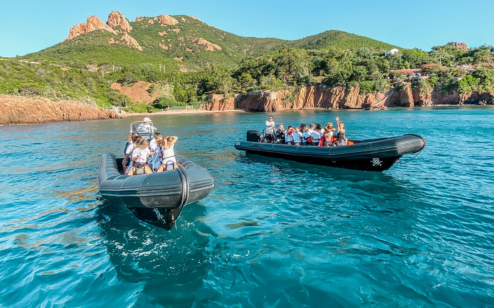 Two boats with tourists exploring Estérel natural park's coastline near Cannes.