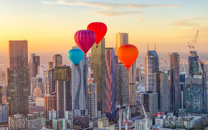 Hot air balloons over Melbourne skyline at sunrise.