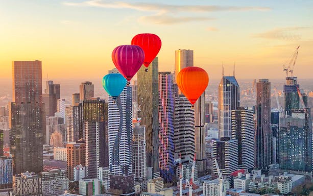 Hot air balloons over Melbourne skyline at sunrise.