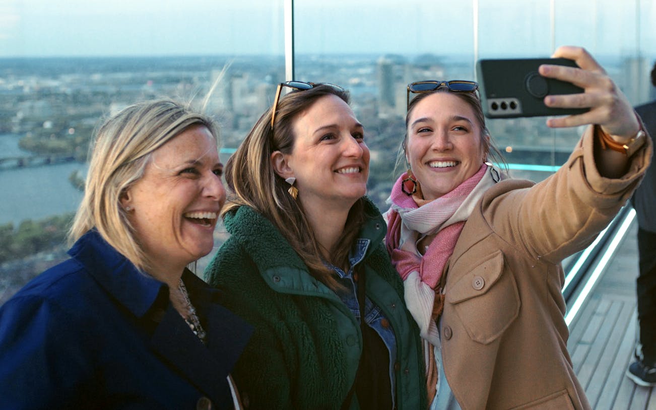 Group taking a selfie on a Boston observation deck with city skyline in the background.