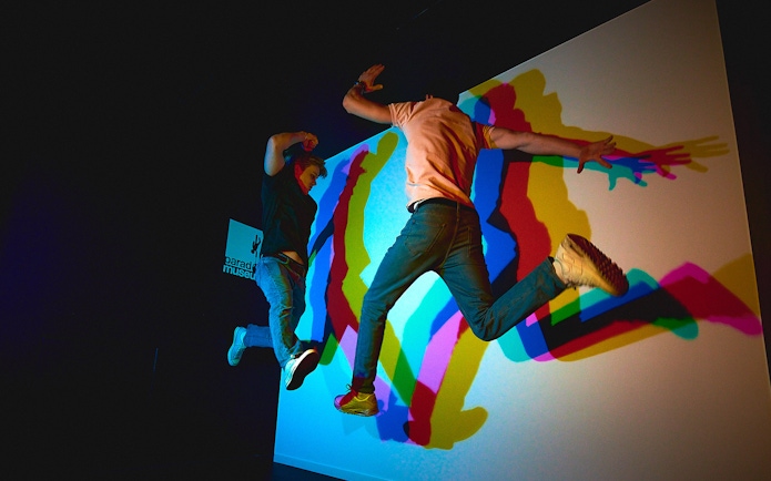 Visitors jumping in front of colorful shadow display at Paradox Museum.
