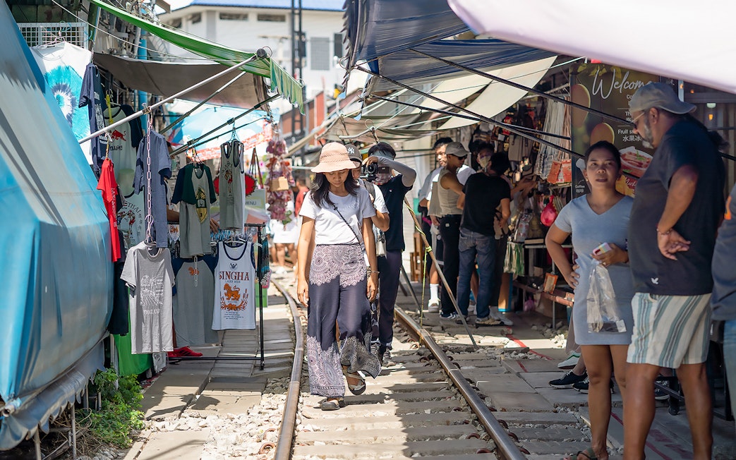 Visitors walking along Maeklong Railway Market with stalls and clothing displays.