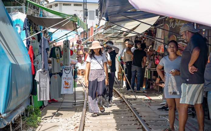 Visitors walking along Maeklong Railway Market with stalls and clothing displays.