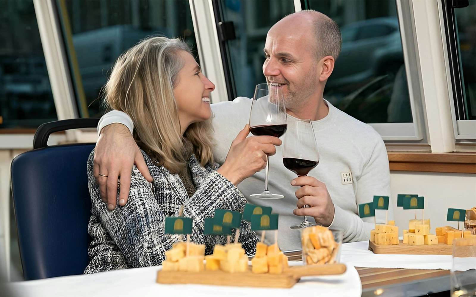 Couple enjoying wine and cheese on an Amsterdam canal cruise at sunset.