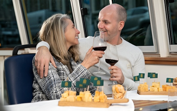 Couple enjoying wine and cheese on an Amsterdam canal cruise at sunset.