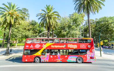 Red double-decker bus for Malaga hop-on hop-off tour near palm trees.