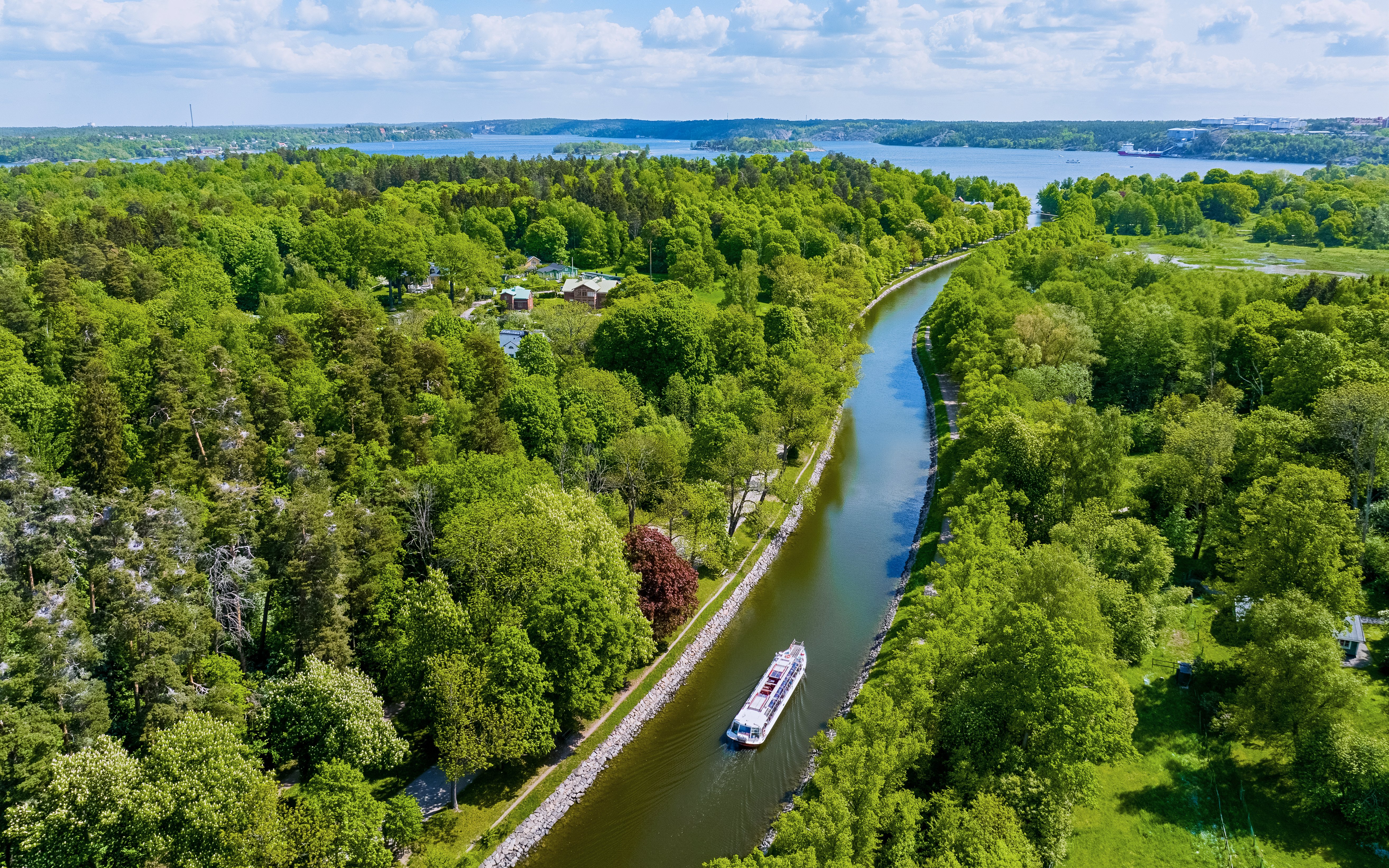 Sightseeing boat cruising on Djurgarden Canal, surrounded by lush greenery in Stockholm, Sweden.