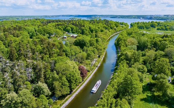 Sightseeing boat cruising on Djurgarden Canal, surrounded by lush greenery in Stockholm, Sweden.