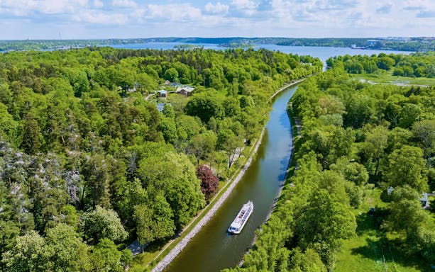 Sightseeing boat cruising on Djurgarden Canal, surrounded by lush greenery in Stockholm, Sweden.