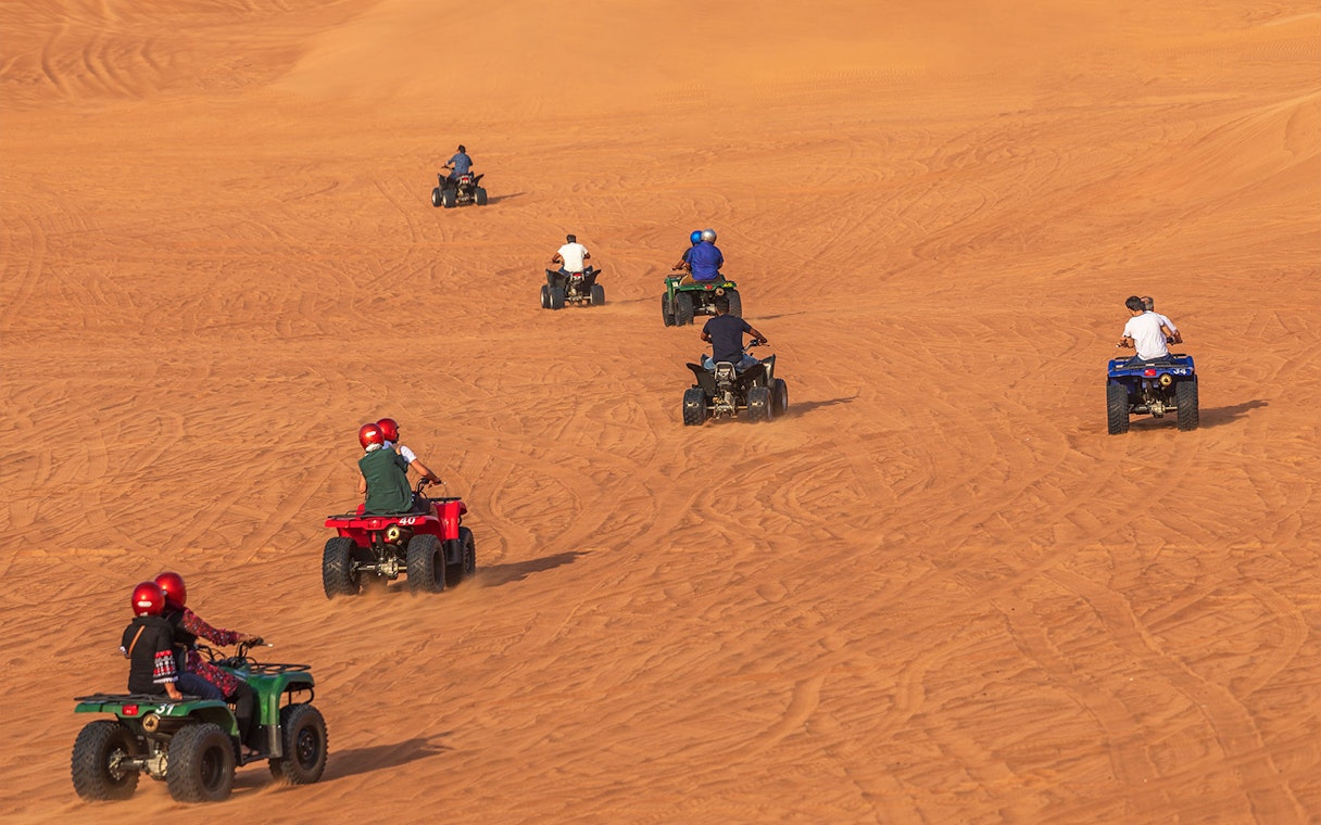 People riding quad bikes on sand dunes during a desert safari in Dubai.