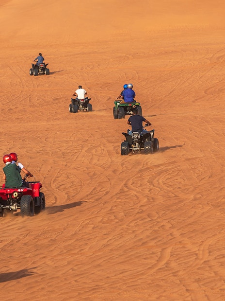 People riding quad bikes on sand dunes during a desert safari in Dubai.