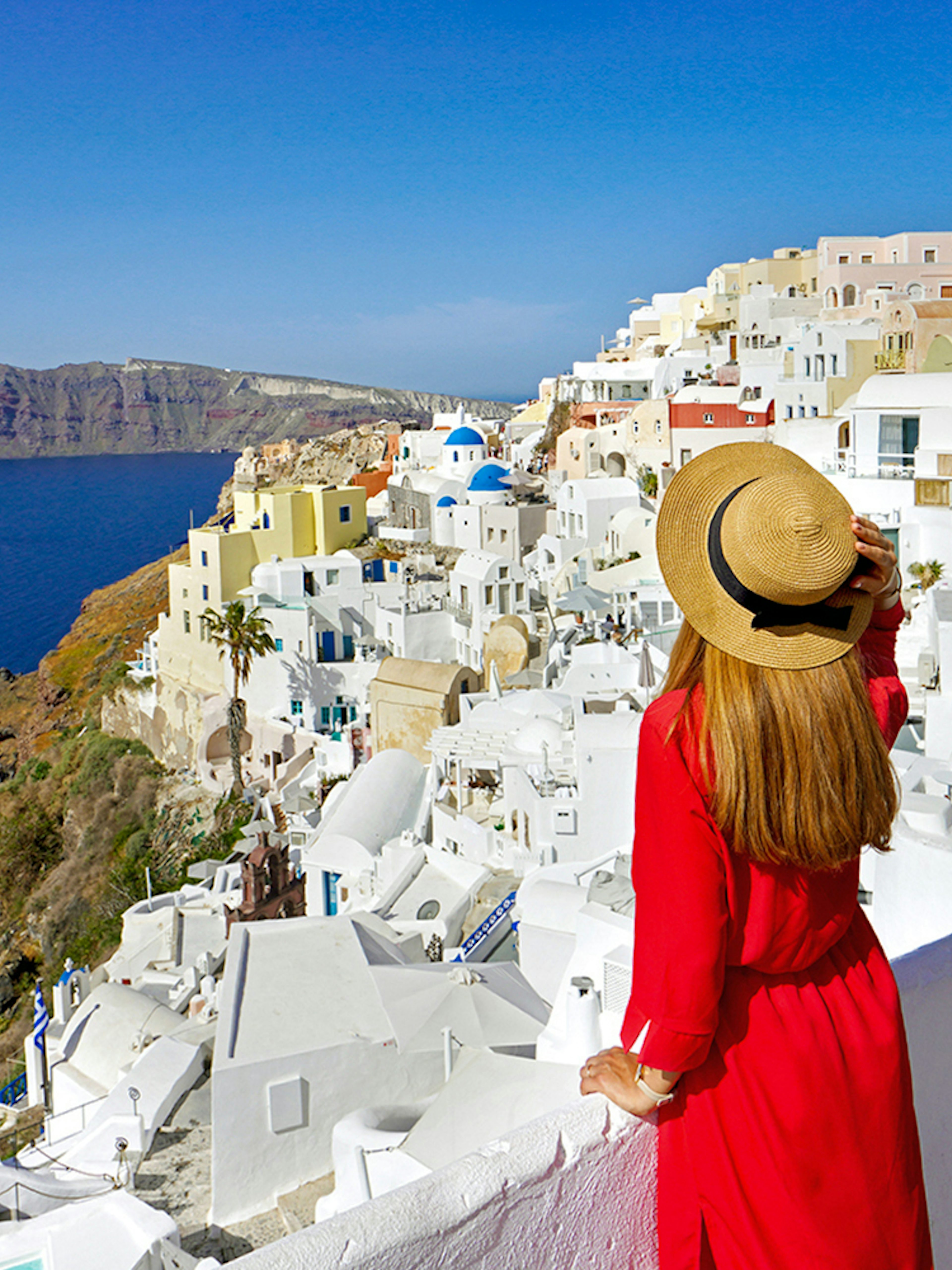 Woman in red dress overlooking white buildings and sea in Oia, Santorini.