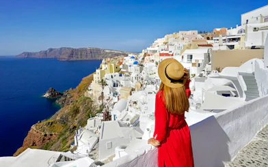 Woman in red dress overlooking white buildings and sea in Oia, Santorini.